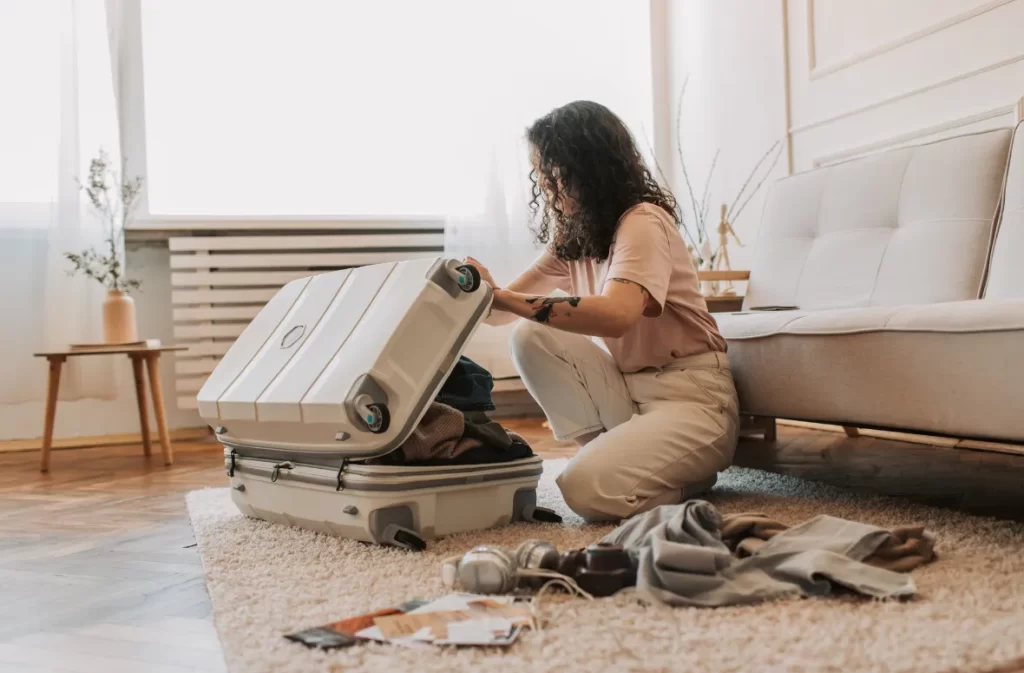 A woman kneeling on a rug, packing a suitcase with travel essentials – what is day packing for a short trip?