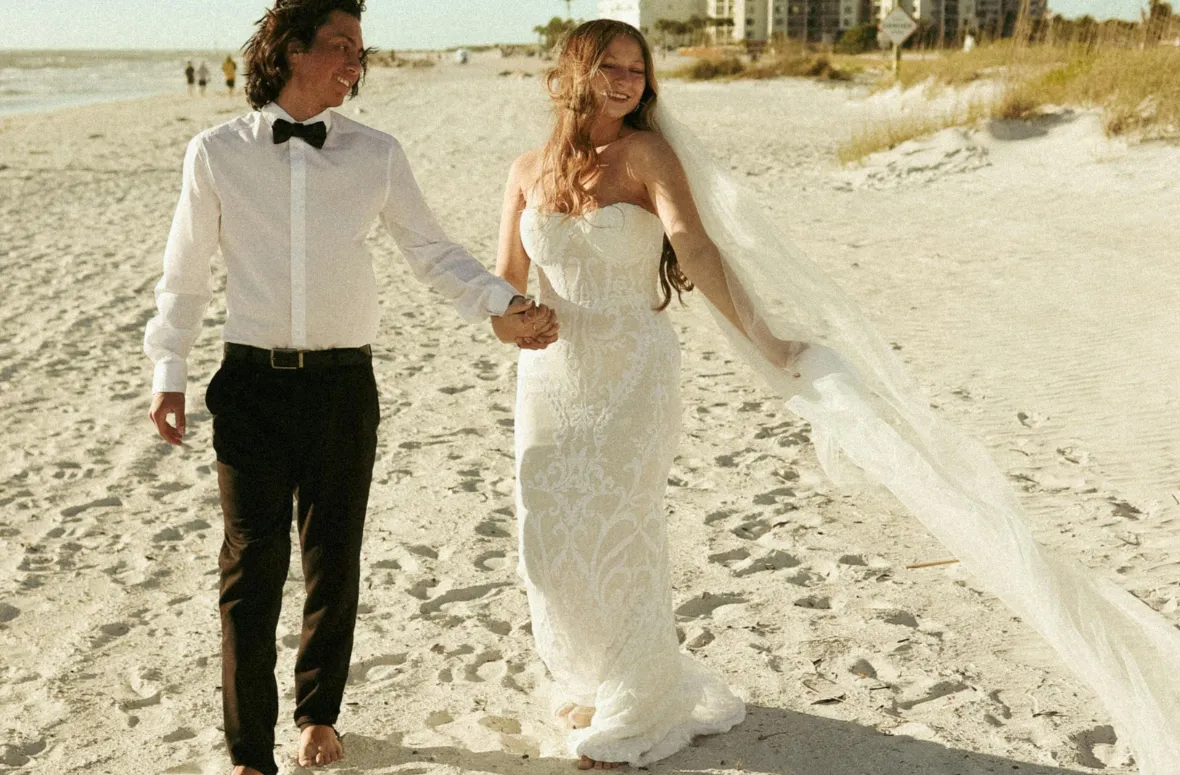 A couple eloping on a sunny beach, holding hands and smiling, embracing their special moment.