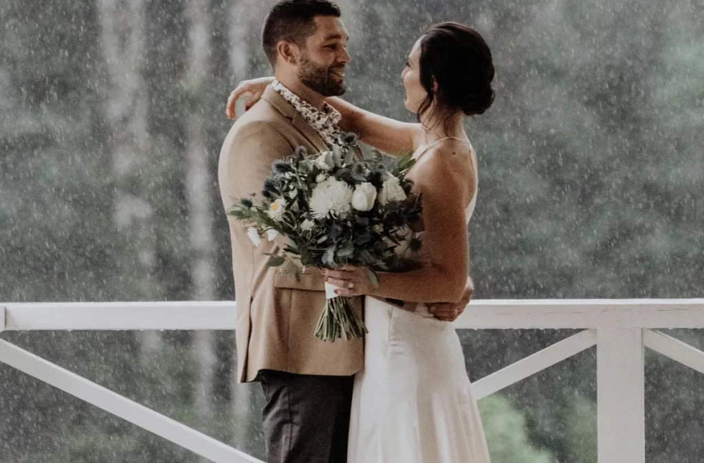 A romantic elopement in the rain, with a couple embracing under a cozy porch, symbolizing intimate love.