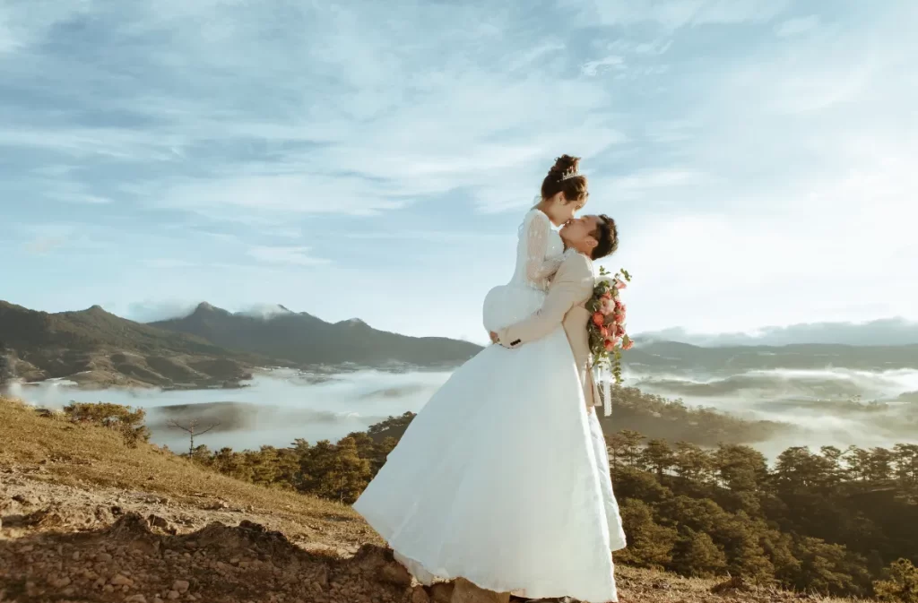 A mountaintop elopement with a couple embracing against a scenic backdrop of misty hills and sunrise.